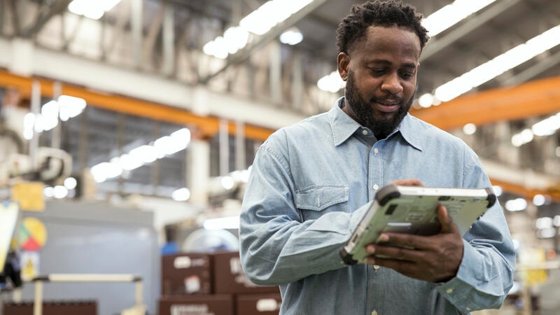 A Male Production Control Manager using a digital tablet in the production line to remote asset monitoring , asset health for reduce production downtime.