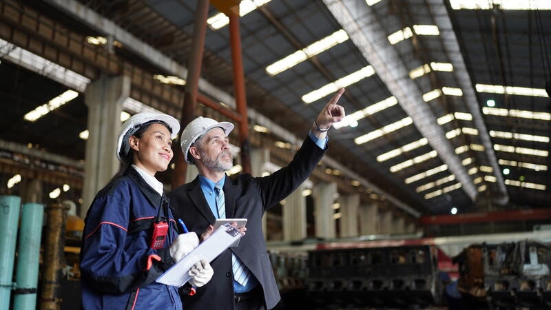 Factory manager or businessman and female engineer in factory. elegant man inspecting factory in industry plant background.